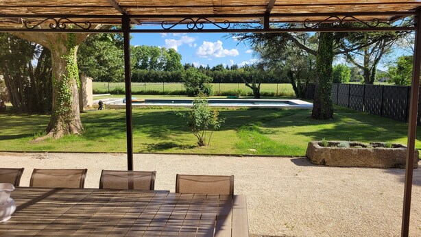 An outdoor patio with a table and chairs, a pergola, a pool, and a grassy yard with trees. - House in Provence, large garden and swimming pool ( 10 people ) in Orange (Orange)