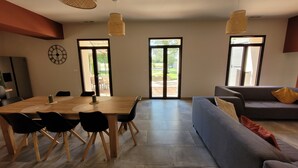 A modern living room with a dining area, featuring a large wooden table, black chairs, a grey sofa, and large windows with a view of the outdoors. - House in Provence, large garden and swimming pool ( 10 people ) in Orange (Orange)