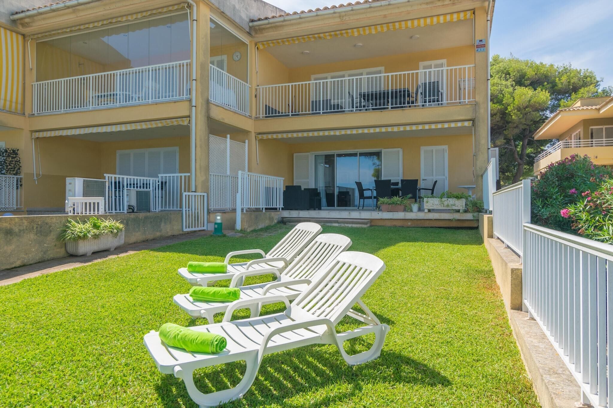 A two-story building with a balcony on the upper floor and a patio area with white lounge chairs and a table.