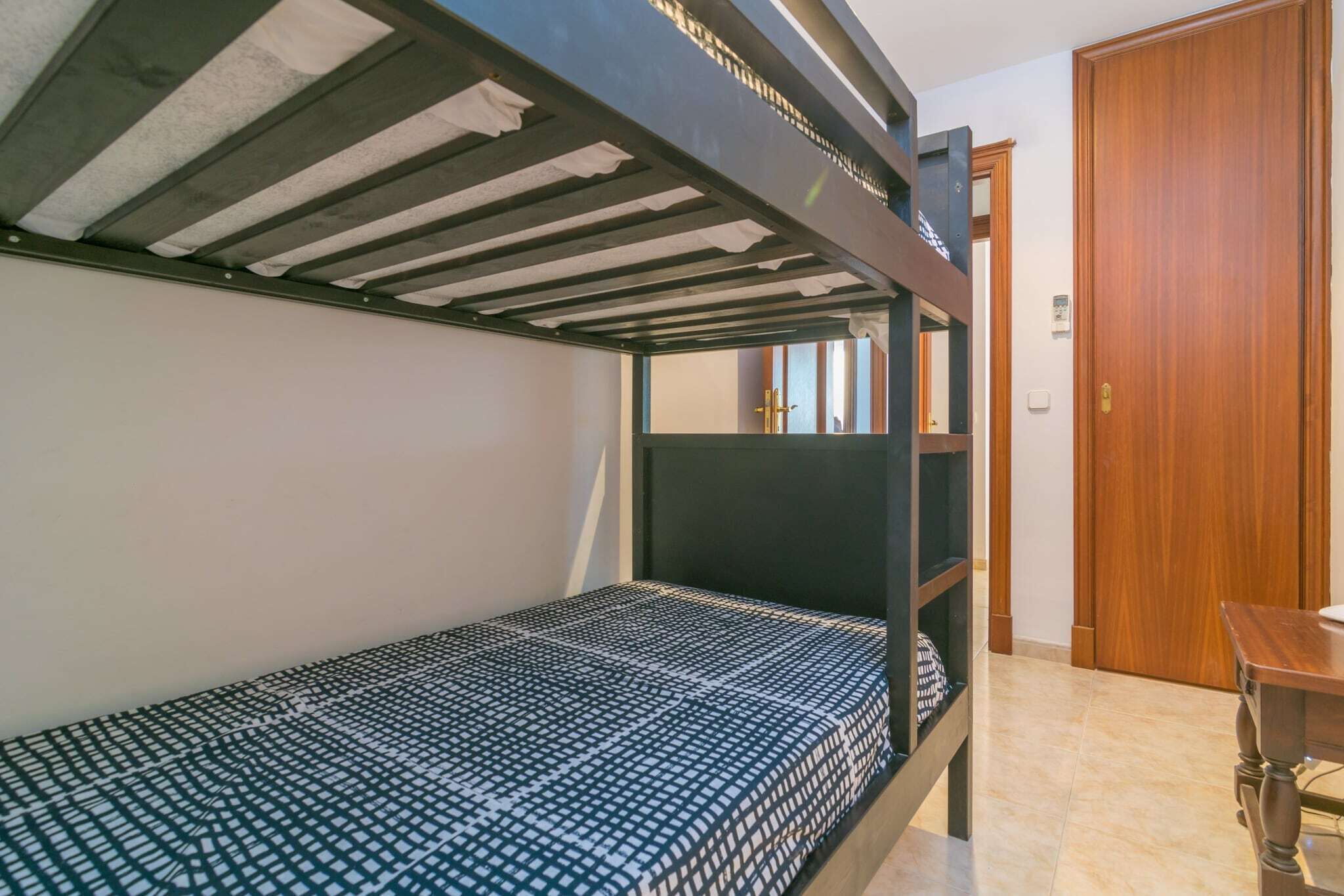 Een slaapkamer met een stapelbed, een houten deur en een klein tafeltje.