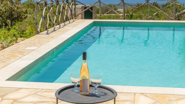 Piscina con una botella de vino y dos vasos sobre una mesa.