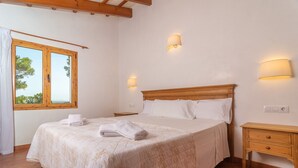 Un dormitorio con una cama grande, dos mesitas de noche, una ventana con cortinas e iluminación en la pared.