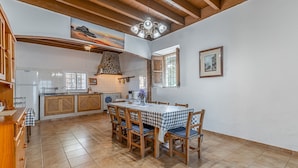 A spacious kitchen with a dining area, wooden cabinets, a stone fireplace, and a large window. - Cas Consul - Villa With Private Pool. Free Wifi (Sant Miquel De Balasant, Illes Balears)