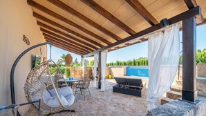 A covered outdoor patio with stone flooring, a hanging chair, a table with chairs, and a view of a swimming pool. - Finca Son Colom (finca Sun Club Home) - Villa (Llucmajor, Illes Balears)