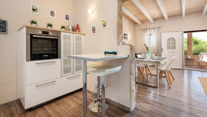 A modern kitchen with white cabinetry, a built-in oven, and a bar area with stools. - Finca Son Colom (finca Sun Club Home) - Villa (Llucmajor, Illes Balears)