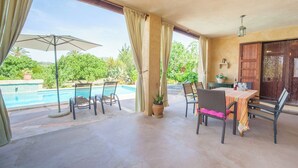 Um alpendre coberto com piscina, área de estar externa e mesa posta para refeições.
