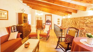Uma sala de estar acolhedora com vigas de madeira, uma parede de pedra e um espaço de jantar com uma mesa posta para dois.
