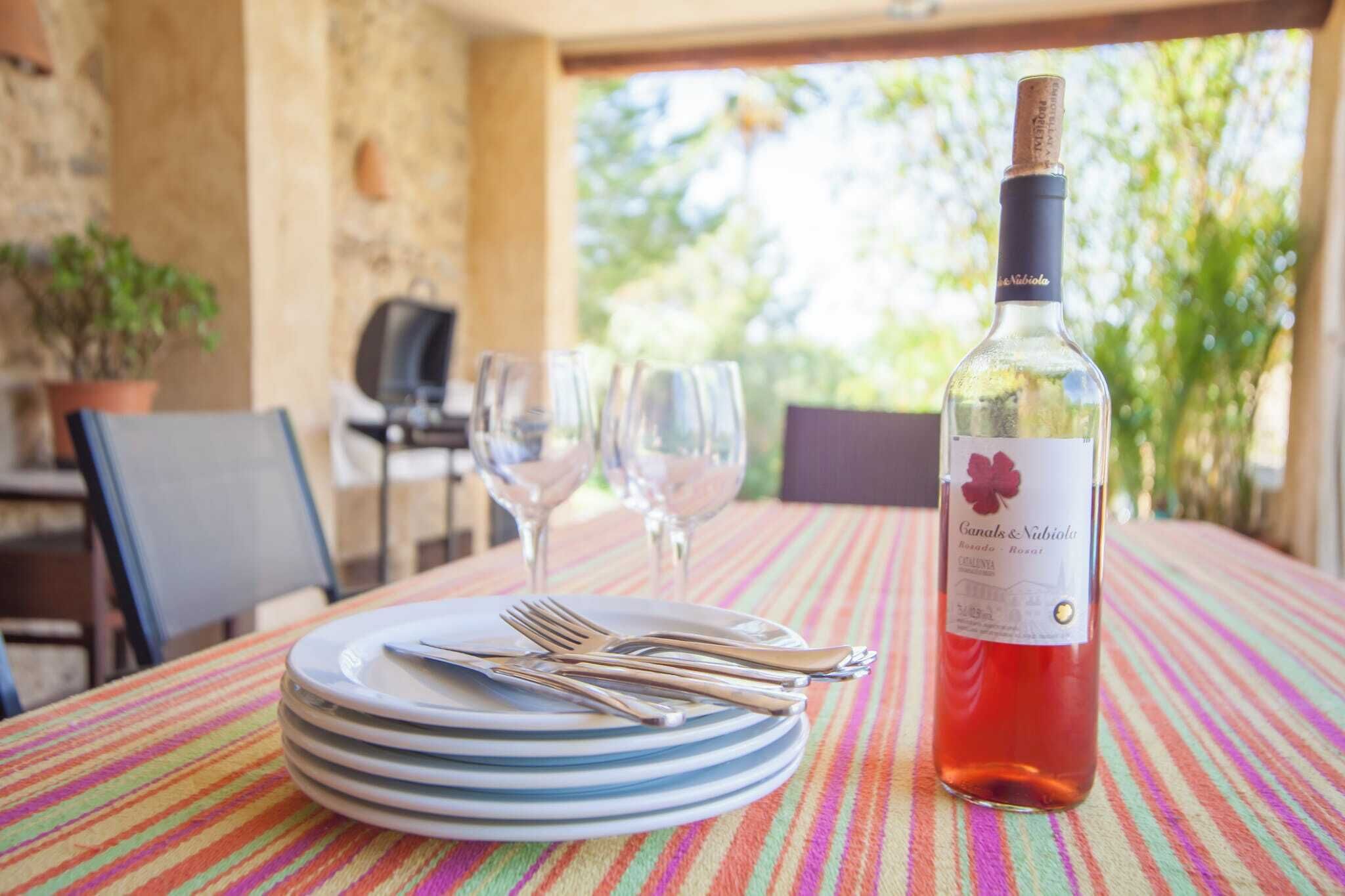 Une table dressée avec des assiettes, des couverts et une bouteille de vin, avec en arri ère-plan une vue sur la verdure et un mur de pierres.