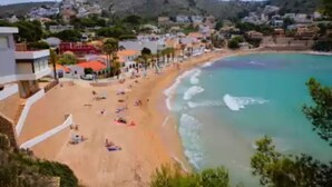 A coastal town with a sandy beach, buildings along the shore, and a mountainous backdrop.