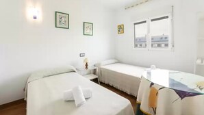 A room with two beds, a small table, a lamp, and a window with a view.