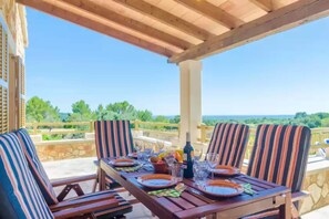 A wooden table set for dining with striped chairs, a stone wall, and a view of the landscape. - S'aresta Den Rumbet - Villa With Private Pool (Llucmajor, Illes Balears)