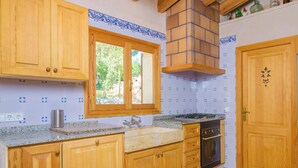 A kitchen with wooden cabinets, a window, a stove, and a tiled backsplash. - S'aresta Den Rumbet - Villa With Private Pool (Llucmajor, Illes Balears)