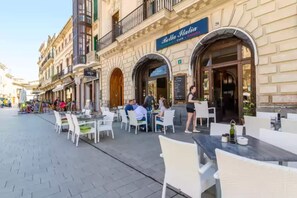 An outdoor cafe with tables and chairs, a sign for 'Bella Italia', and a building facade with arched windows and balconies. - S'aresta Den Rumbet - Villa With Private Pool (Llucmajor, Illes Balears)