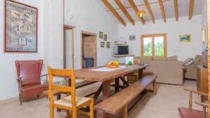 A dining area with wooden benches and chairs, a table with a fruit bowl, a sofa, and a TV. - S'aresta Den Rumbet - Villa With Private Pool (Llucmajor, Illes Balears)