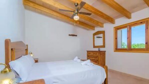 A bedroom with a bed, wooden headboard, bedside lamp, ceiling fan, wooden dresser, and a window with a view of greenery. - S'aresta Den Rumbet - Villa With Private Pool (Llucmajor, Illes Balears)
