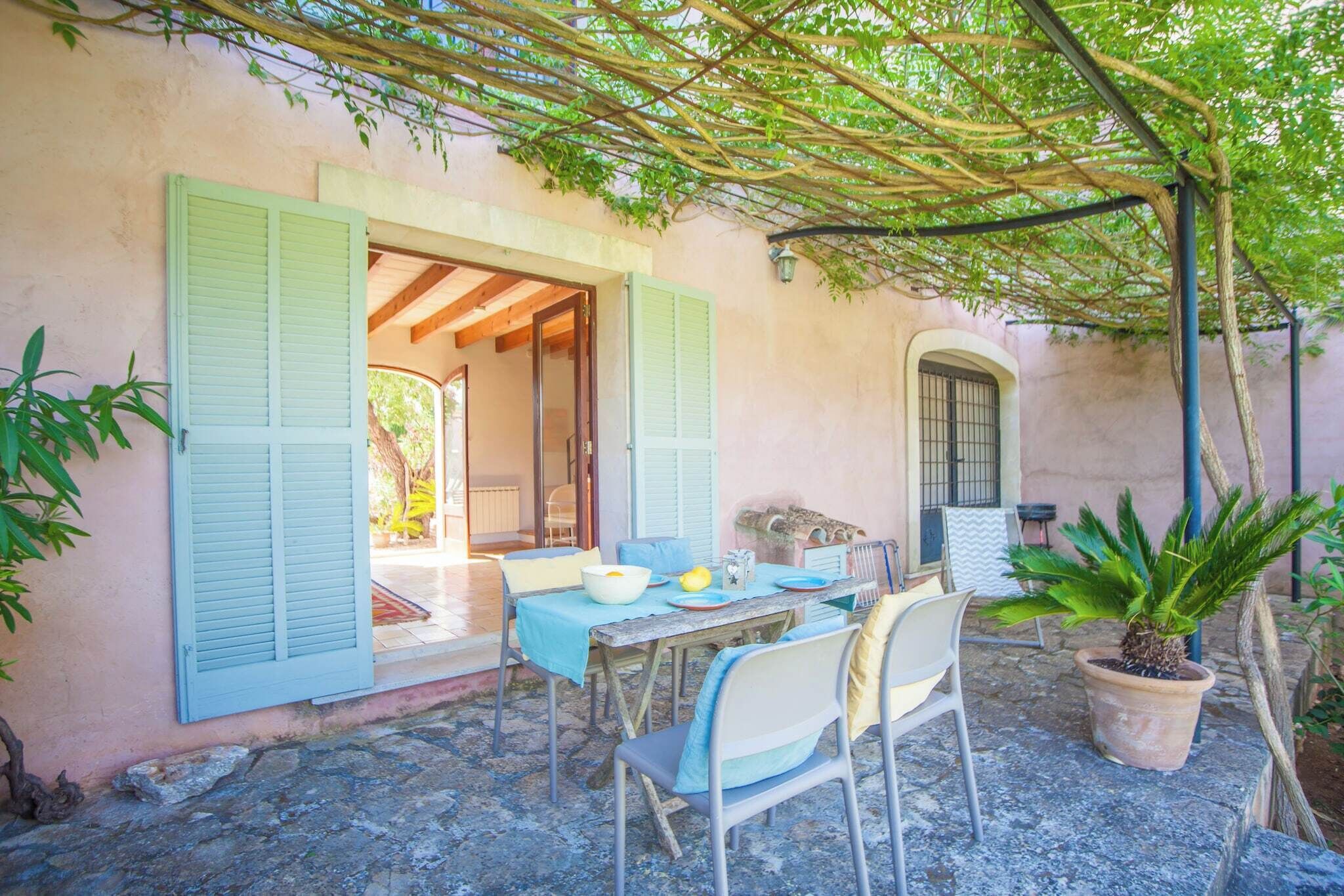 Un espace de restauration en plein air avec une table dressée pour deux personnes, une plante en pot et un patio couvert agrémenté d’une pergola.