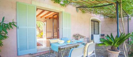 Un espace de restauration en plein air avec une table dressée pour deux personnes, une plante en pot et un patio couvert agrémenté d’une pergola.
