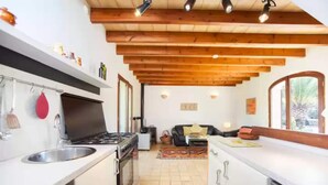 Una cucina moderna con piano cottura a gas, lavello e pensili bianchi. Il soffitto in legno presenta travi a vista e una finestra che lascia entrare luce naturale.