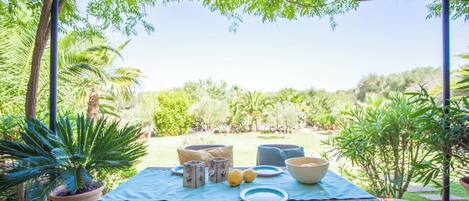 Un espace de restauration en plein air, avec une table dressée pour un repas, entouré d’une végétation luxuriante et surmonté d’une pergola.
