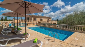 A swimming pool with lounge chairs and umbrellas, surrounded by stone tiles and a building with a balcony. - Es Rafal Cogolles - Villa With Private Pool (, Illes Balears)