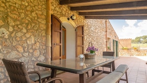 A stone-walled patio with a glass-top table, wicker chairs, and a bench. - Es Rafal Cogolles - Villa With Private Pool (, Illes Balears)