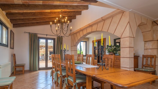 A dining area with a wooden table, chairs, a chandelier, and a view through an archway. - Es Rafal Cogolles - Villa With Private Pool (, Illes Balears)