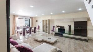 Un salon moderne avec un canapé, une table basse et un téléviseur. Il y a également un coin repas avec des chaises et une table.