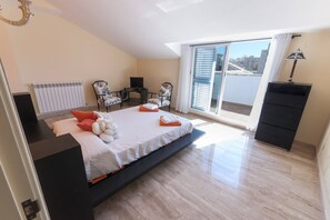 A modern bedroom with a bed, a desk, a chair, and a view of the city through large windows.