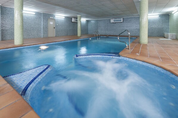 An indoor swimming pool with clear water, tiled walls, and a tiled deck.