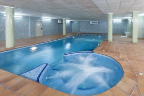 An indoor swimming pool with a hot tub, tiled walls, and a tiled floor.