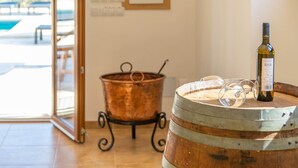 A wine barrel with a bottle and glasses on top, a copper pot on a stand, and a view of an outdoor area with tables and chairs. - Son Roca - Villa With Private Pool In Montuïri (Montuïri, Illes Balears)