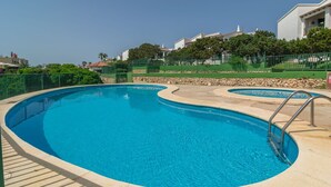 Una piscina de diseño curvo, rodeada por un muro de piedra y una valla verde.