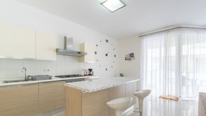 A modern kitchen with a central island, bar stools, a clock, and a large window with sheer curtains. - Amazing and Spacious Apartmet wSide Sea View (San Pawl il-Baħar)