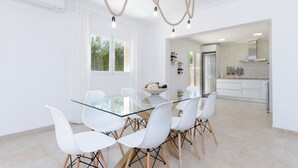 A modern kitchen with white cabinetry, a stainless steel refrigerator, and a glass dining table with white chairs. - Dones D'aigua 11 - Villa With Private Pool (S'estanyol (colònia De Sant Pere), Illes Balears)