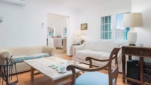 Sala de estar con dos sofás, una mesa de centro y una lámpara. Se ve una cocina al fondo.