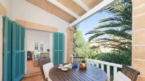 Un patio con una mesa redonda de madera, sillas y una pequeña mesa dispuesta con tazas y una cesta de fruta.