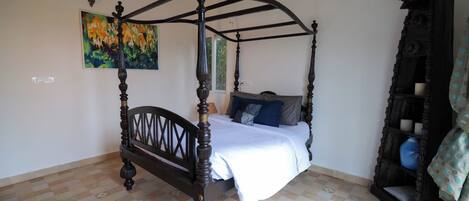 Uma cama de dossel com colcha branca, um quadro na parede e um chão estampado.