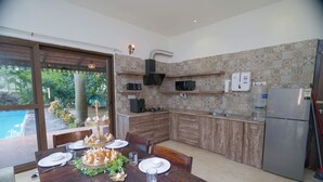 Una cocina moderna con armarios de madera, microondas integrado y refrigerador. Hay una mesa de comedor con platos, vasos y velas.