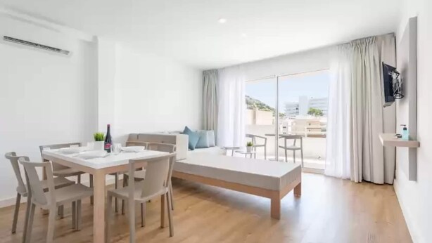 Una habitación moderna y bien iluminada con una mesa de comedor, sillas, un sofá y un televisor montado en la pared.