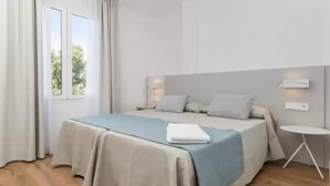 Una habitación de hotel moderna con una cama grande, una mesita de noche pequeña y un ventanal con cortinas.