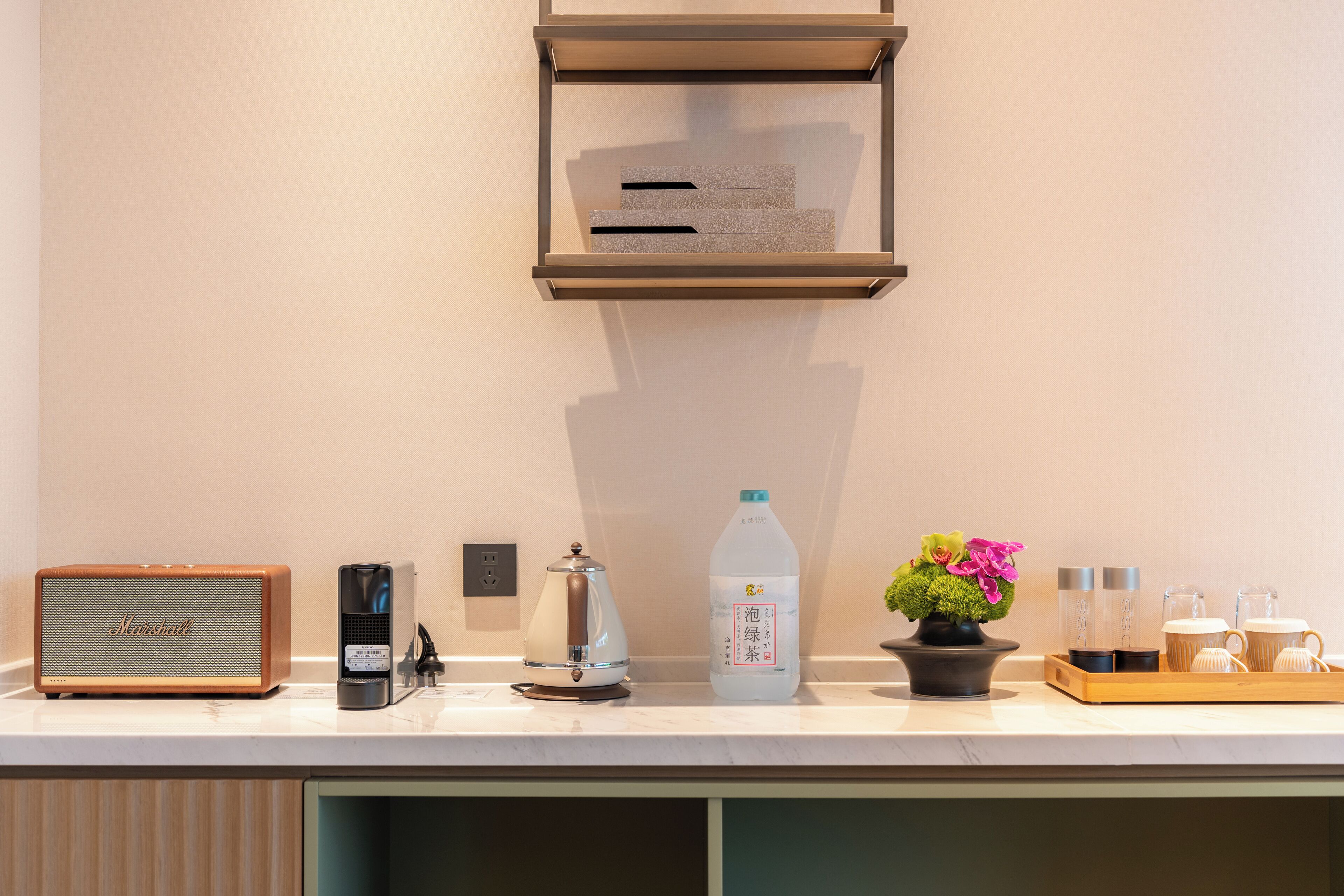 A kitchen counter with a coffee maker, a kettle, a bottle of milk, a potted plant, and a tray with cups and a teapot.