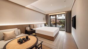 A modern hotel room with a large bed, a sofa, a dining table with tea set, a TV, and a balcony with a view of the outside. - The Serene House (Hangzhou)