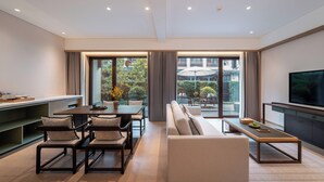 A modern living room with a sofa, dining table, and chairs, large windows, and a flat-screen TV. - The Serene House (Hangzhou)