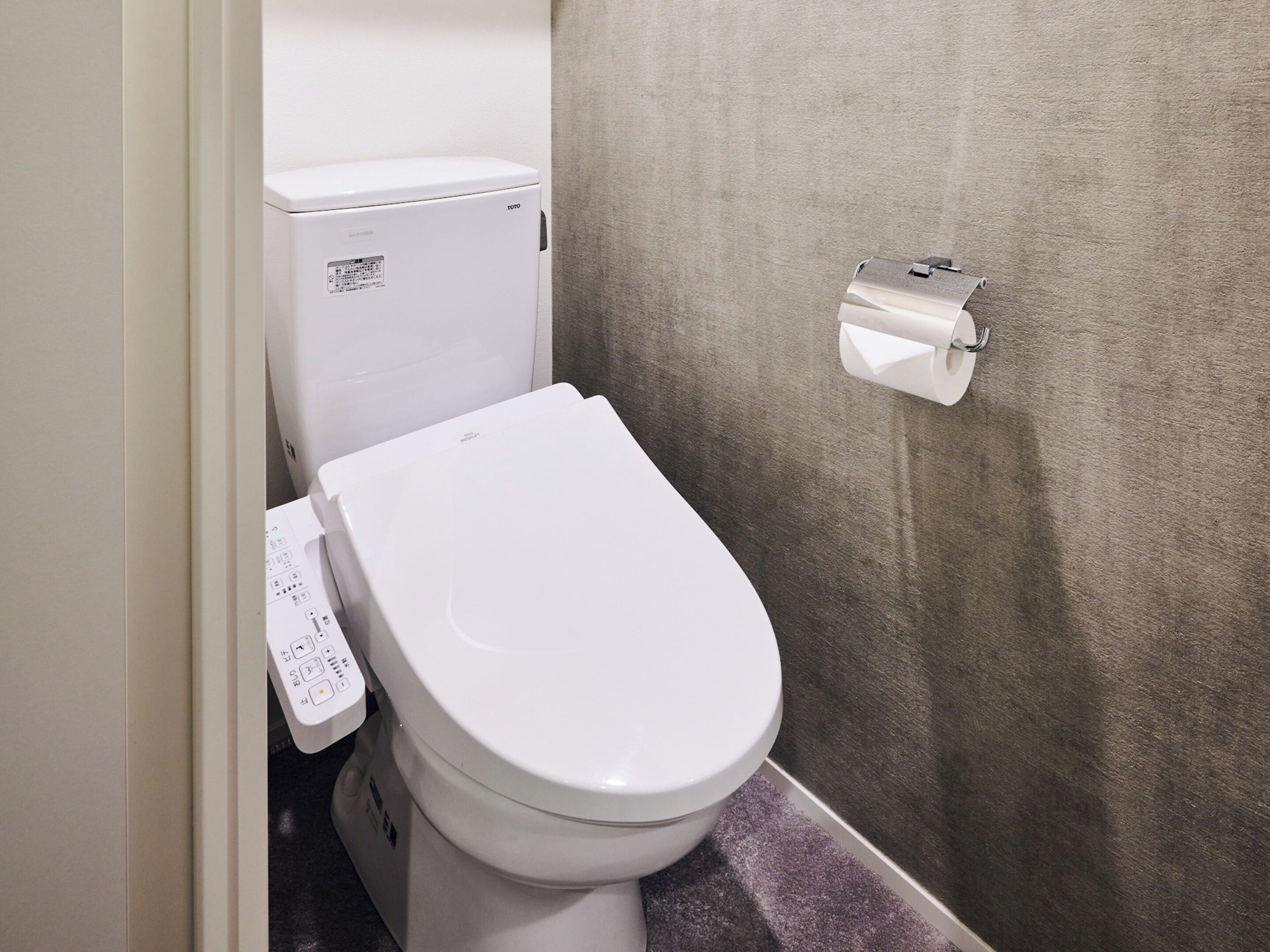 A white toilet with a control panel and a toilet paper holder on the wall.