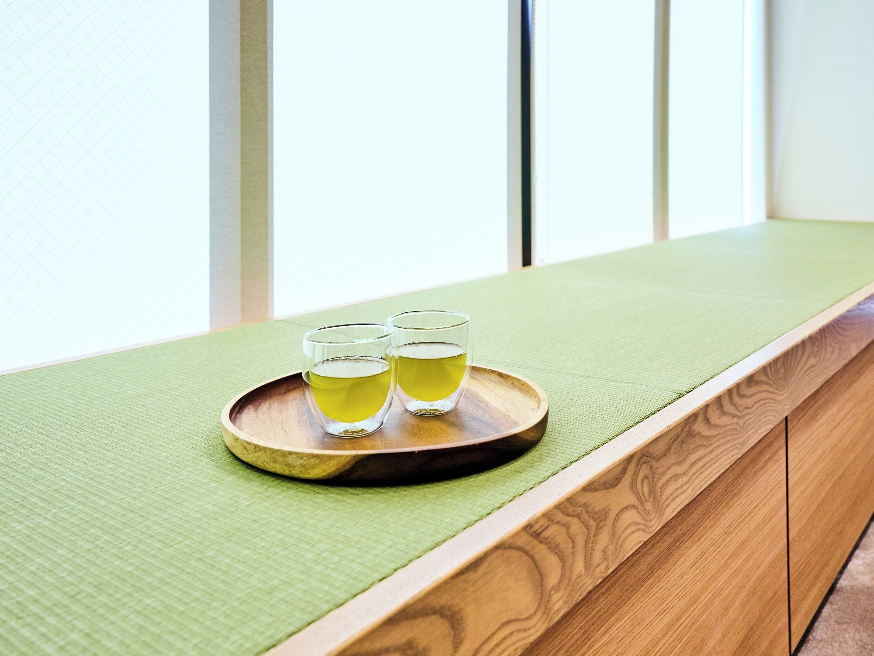 A wooden bench with a green cushion and a wooden tray holding two glasses of tea.