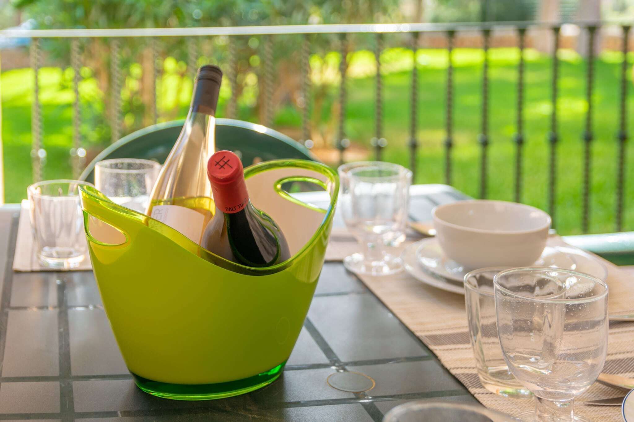 A table with a green bowl containing a bottle, clear glasses, and a white bowl.