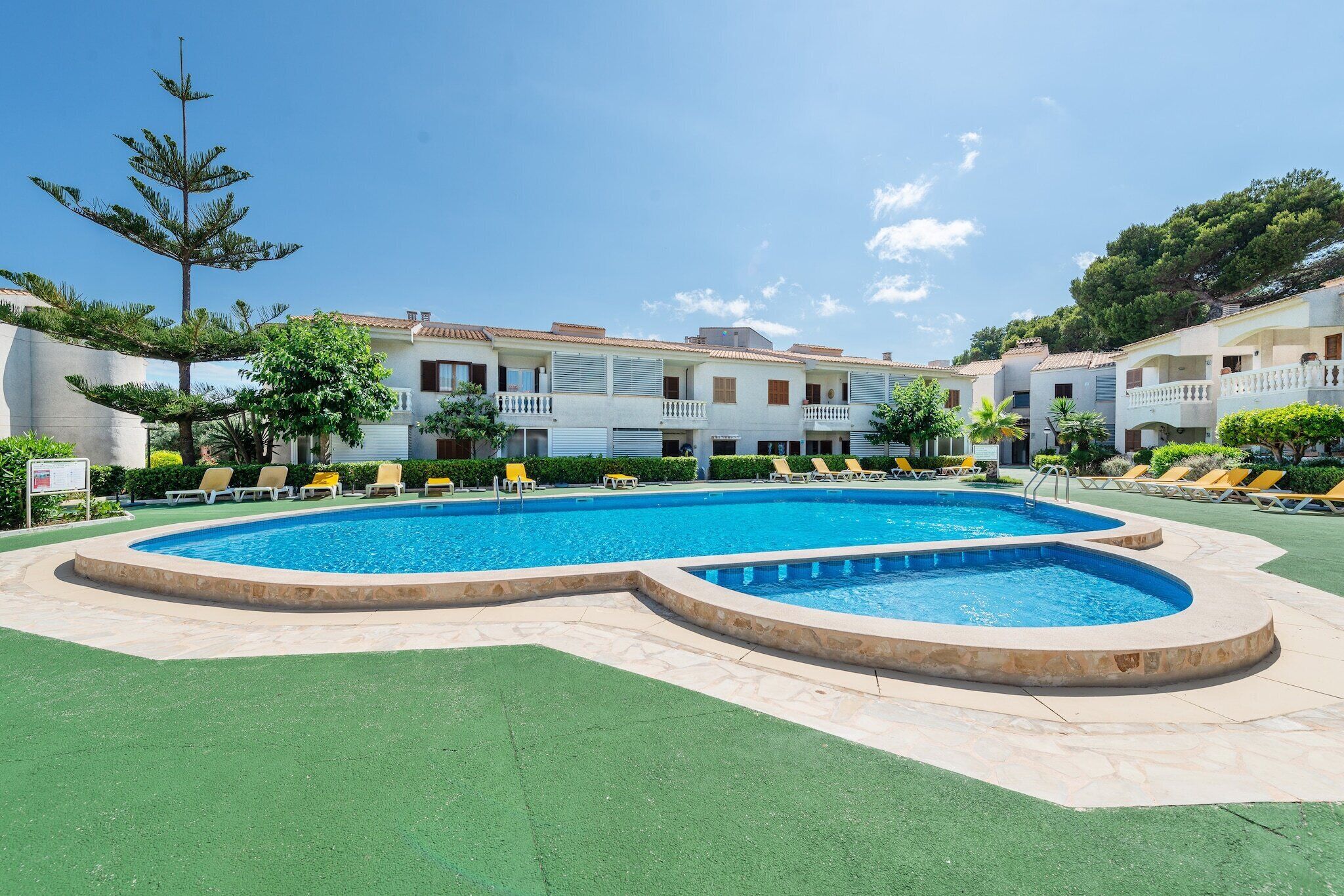 A swimming pool with multiple lanes, surrounded by lounge chairs and a building with balconies.