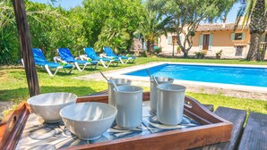 Escena junto a la piscina con sillas de descanso, una piscina y una bandeja con recipientes y tazas.
