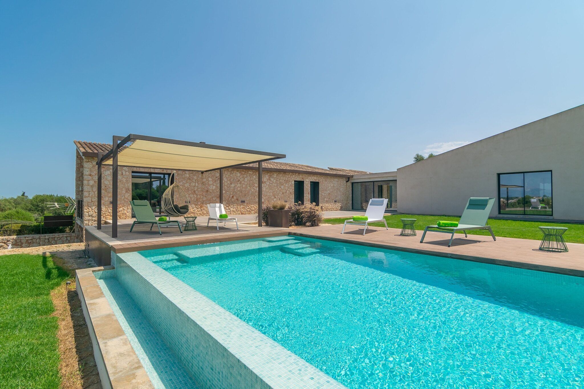 Une piscine extérieure moderne, dotée de chaises longues et d’un patio couvert.