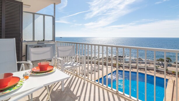 A balcony with a view of the sea, a pool, and a table with a red bowl and plates. - Mar Blava - Apartment In Cala Rajada. Free Wifi (Cala Rajada, Illes Balears)